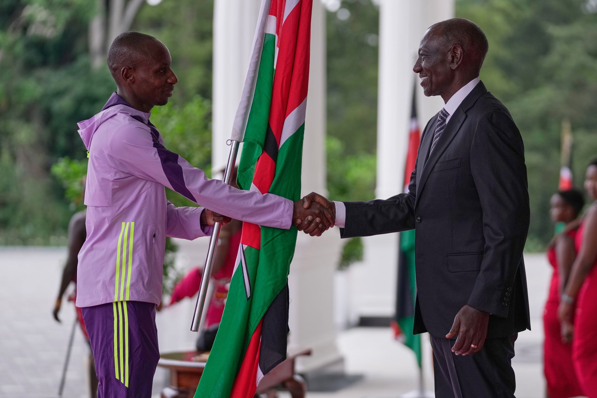 Der kenianische Marathon-Weltrekordler Sabastian Sawe (l) übergibt die kenianische Flagge an Präsident William Ruto.