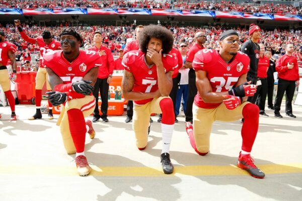 Colin Kaepernick (Mitte) kniend bei der Nationalhymne. Er bekam Unterstützung einiger Mitspieler